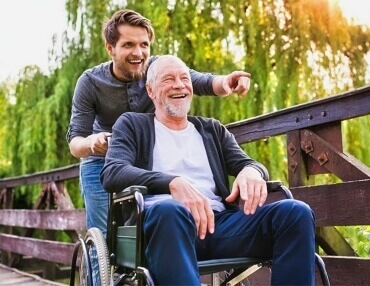 male companion with elderly main in a wheelchair going across a walkbridge